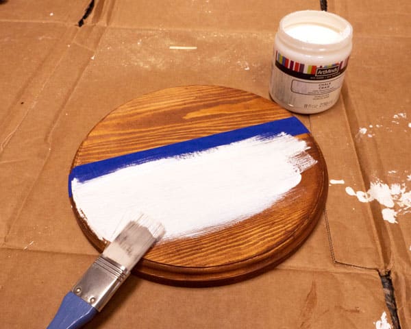 The door round in process of being painted- there is a paint brush and the door round has had half of a first coat