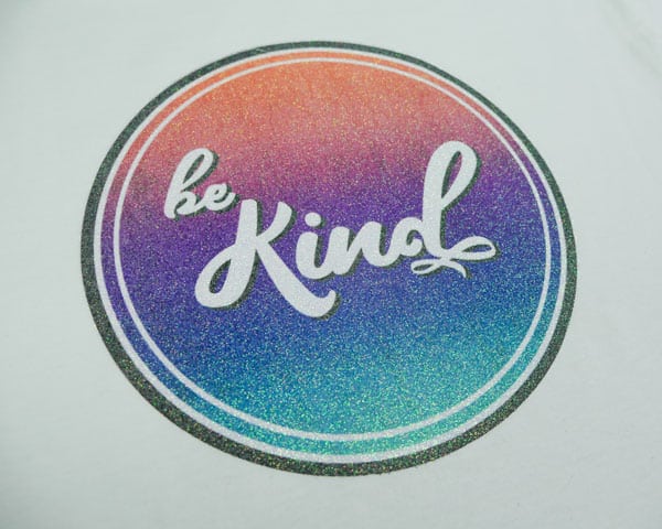 The "Be Kind" sublimation file pressed onto Rainbow Opaque White GlitterFlex® Ultra and on a white shirt